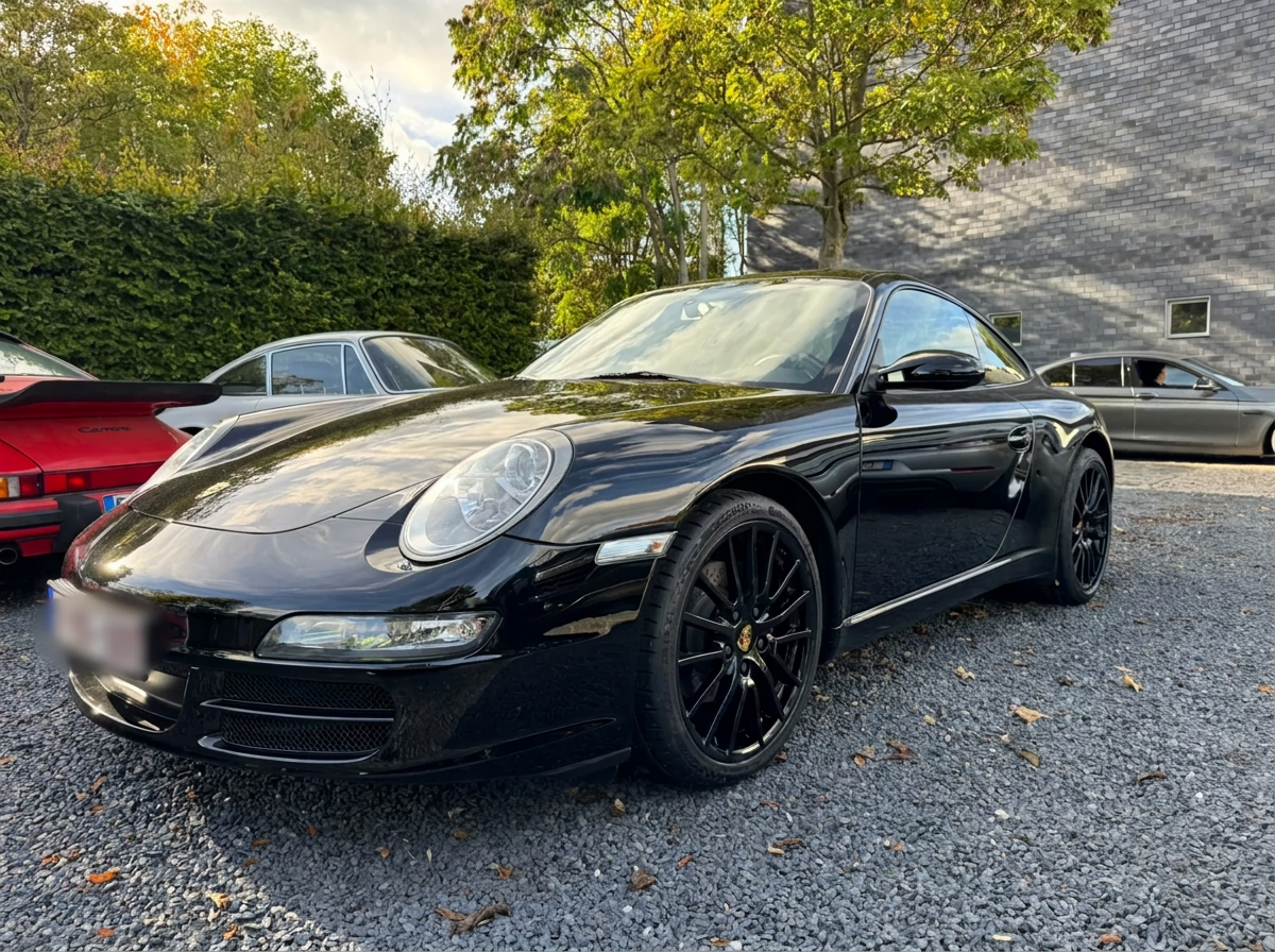 Black Porsche 997 Carrera coupé parked on gravel in autumn light