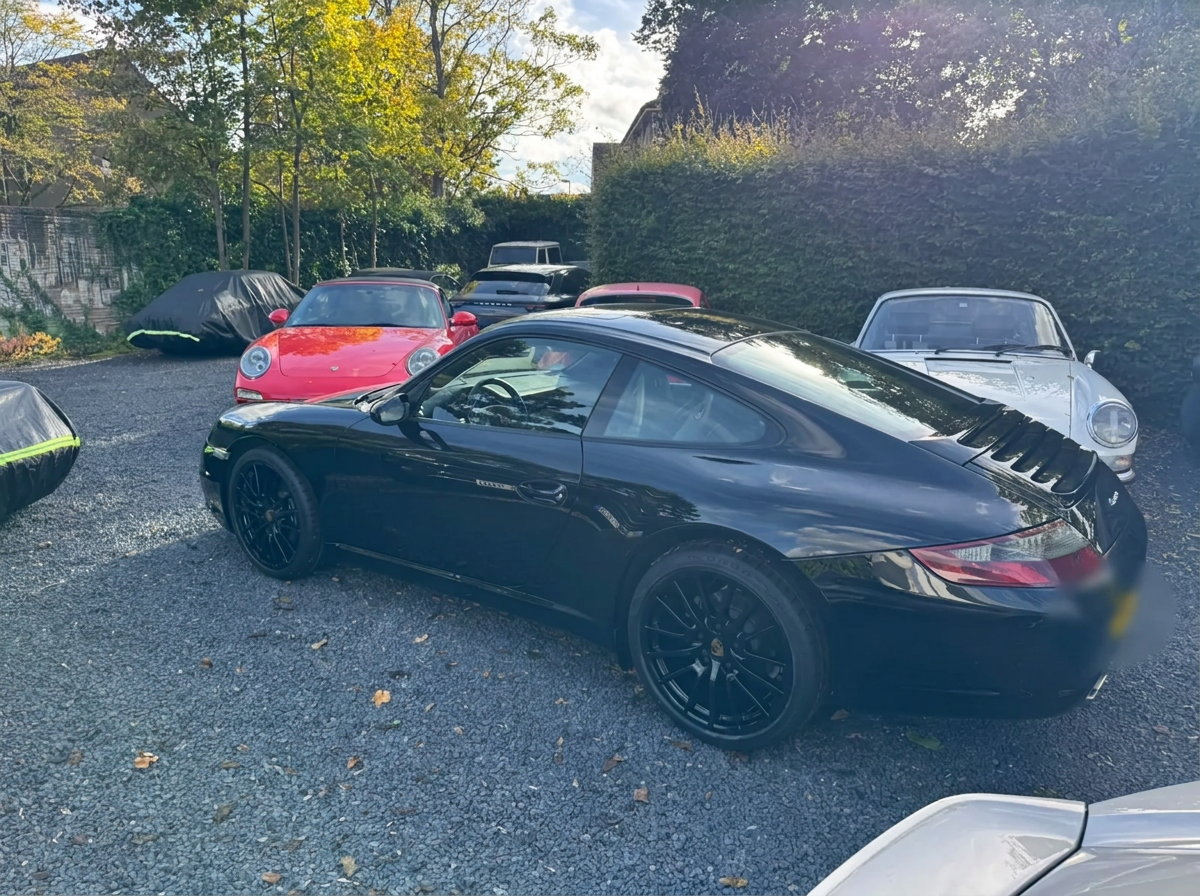 Side view of a black Porsche 997 Carrera among other classic Porsches
